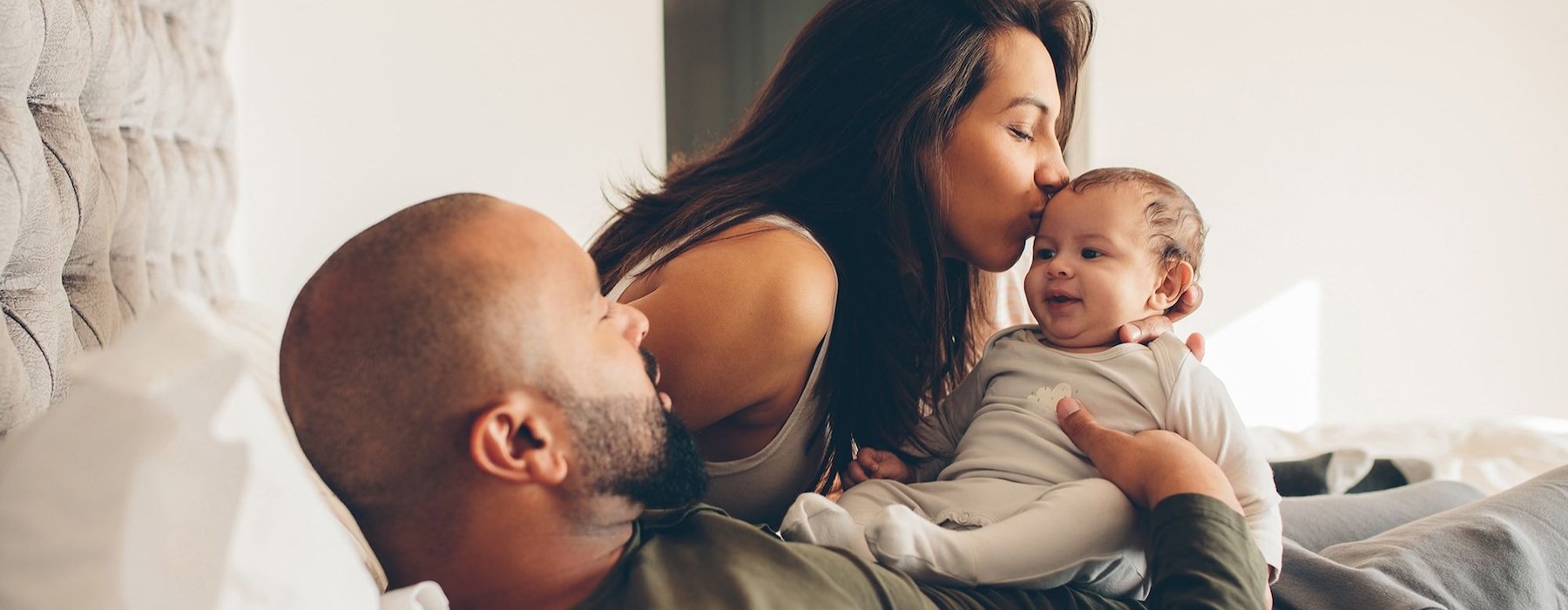 mother kisses her infant while father lies in bed and holds him